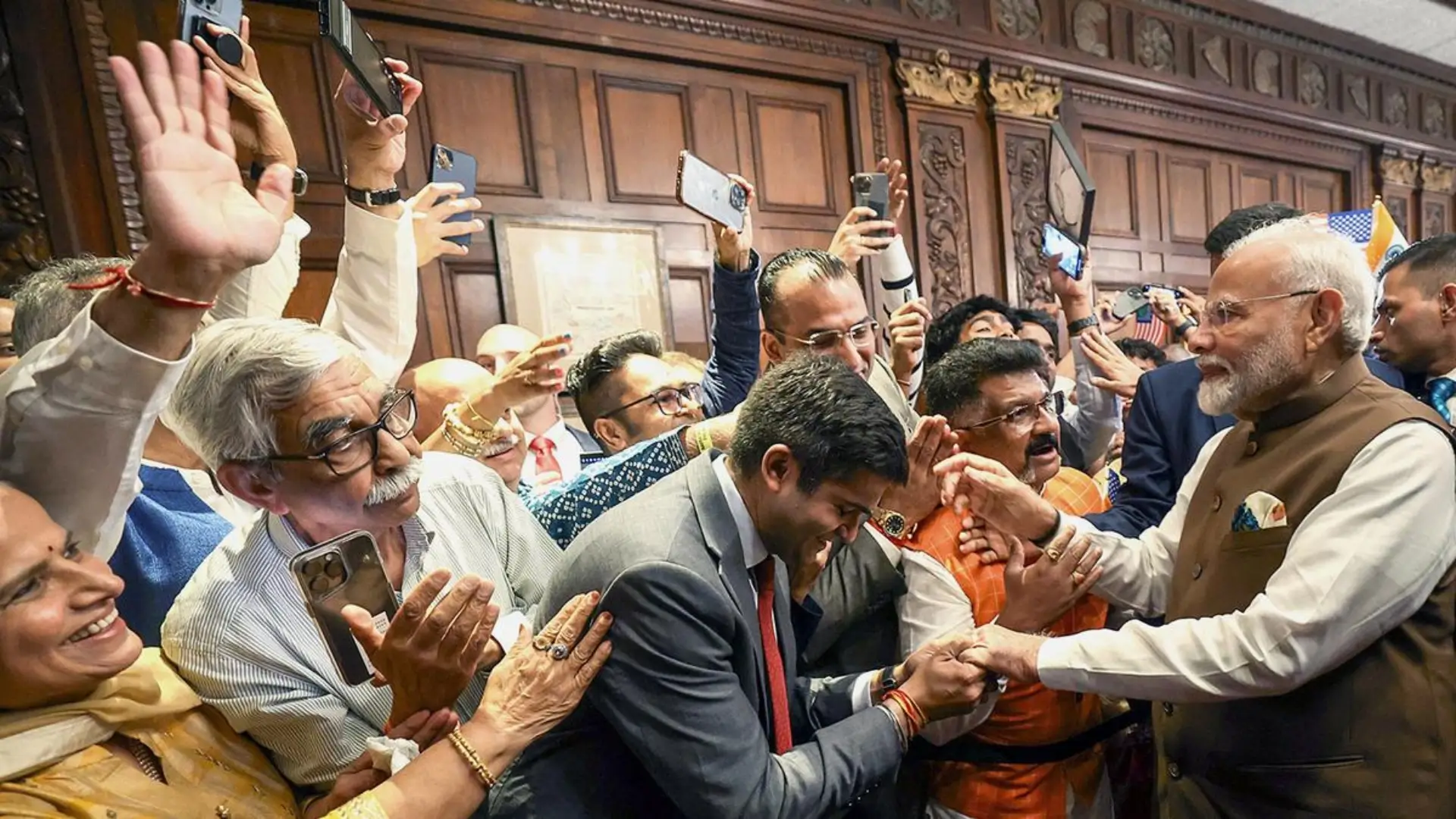 Prime Minister Narendra Modi greets supporters amid a surge of enthusiasm, as onlookers capture the moment on their phones.